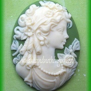 May include: A white cameo featuring a woman with a dragonfly design on a green background. The cameo is 40mm x 30mm.