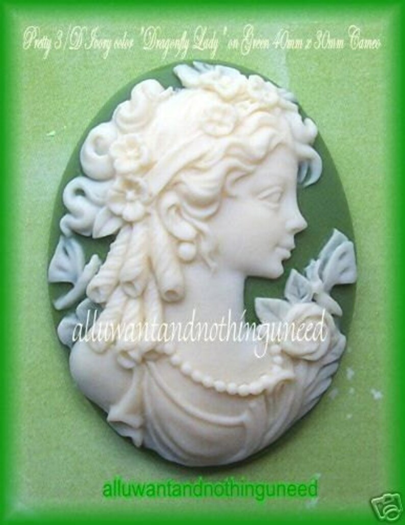 May include: A white cameo featuring a woman with a dragonfly design on a green background. The cameo is 40mm x 30mm.