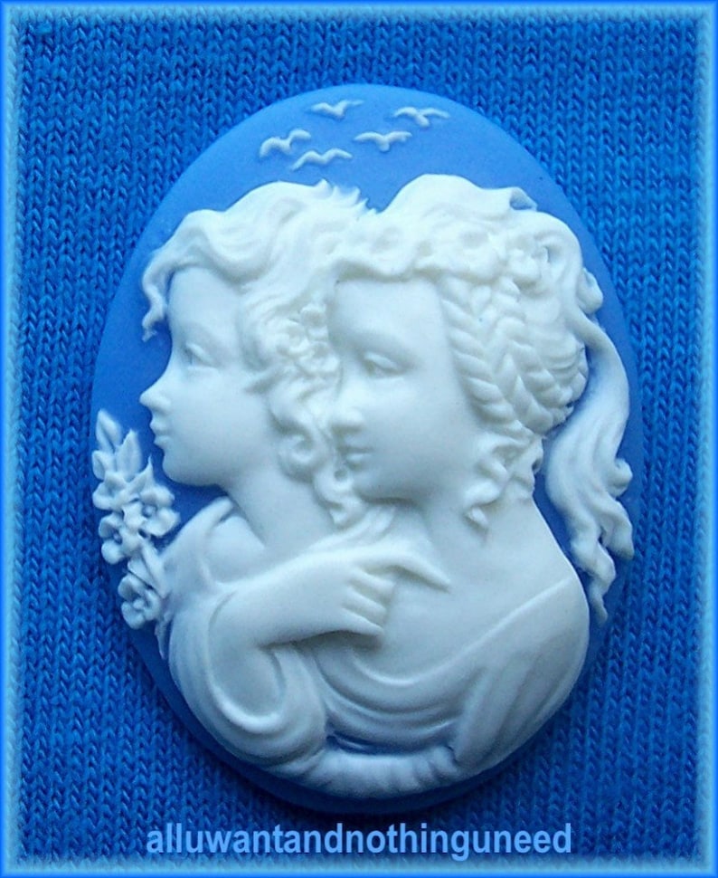 May include: A blue cameo with two white figures of women embracing. The cameo is set against a blue background with white birds flying overhead.