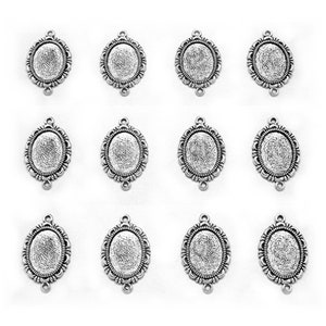 May include: Twelve silver oval-shaped pendant trays with a decorative border. Each tray has three holes for attaching a chain or cord.