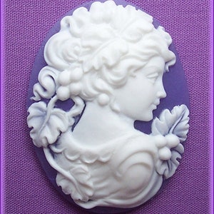 May include: White cameo featuring a woman's profile with a floral design. The cameo is set against a purple background.