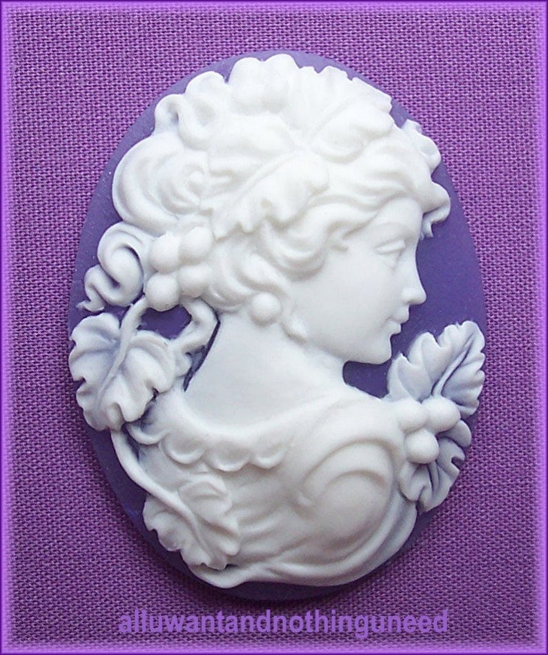 May include: White cameo featuring a woman's profile with a floral design. The cameo is set against a purple background.