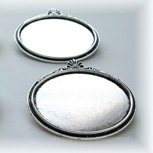 May include: Two silver oval-shaped metal trays with a decorative border and a raised design at the top.
