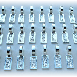 May include: Twenty-four silver-toned metal pendant caps with a textured rectangular design. The caps have a loop at the top for attaching to jewelry.