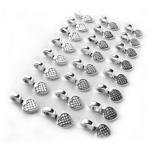 May include: A group of silver heart-shaped pendant clasps with a textured design. The clasps are arranged in a diagonal line on a white background.