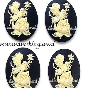 May include: Four oval cameo pendants featuring a cream-colored fairy design on a black background. The fairy is seated on a flower, holding a flower stem. The text "alluwantandnothinguneed" is printed on each pendant.