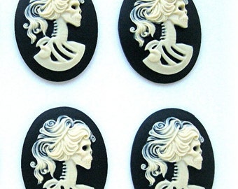 May include: Four black and white cameo-style skull and skeleton head ornaments. The ornaments are oval shaped and feature a detailed skull with a feminine hairstyle.
