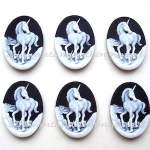 Pu&ograve; includere: Sei ciondoli ovali in cammeo bianco e nero con un unicorno bianco con un corno d'argento. Gli unicorni sono in una posa in piedi con la testa girata di lato. I ciondoli sono su uno sfondo nero.
