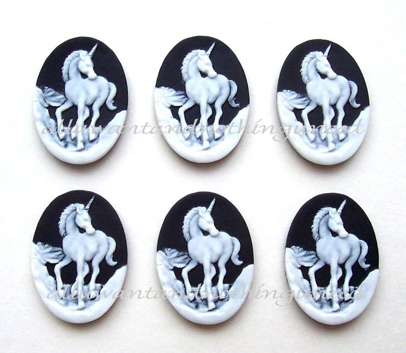 Pu&ograve; includere: Sei ciondoli ovali in cammeo bianco e nero con un unicorno bianco con un corno d'argento. Gli unicorni sono in una posa in piedi con la testa girata di lato. I ciondoli sono su uno sfondo nero.