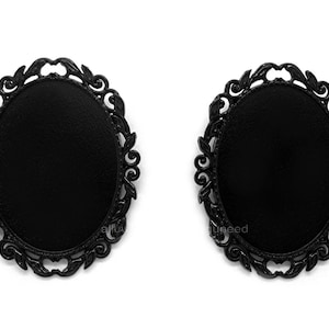 May include: Two black oval-shaped metal frames with ornate scrollwork designs. The frames are blank and ready for a photo or other embellishment.