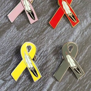 May include: Four enamel pins featuring a ribbon with a feather design. The ribbons are pink, red, yellow, and gray.