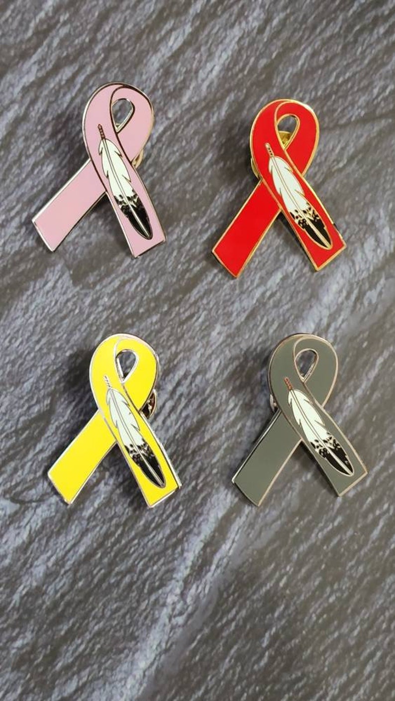 May include: Four enamel pins featuring a ribbon with a feather design. The ribbons are pink, red, yellow, and gray.