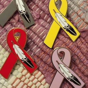 May include: Four enamel pins in the shape of a ribbon with a feather design. The ribbons are gray, yellow, red, and pink.