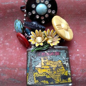 May include: A vintage Texas-themed lighter with a map of the state and a silver finish. The lighter is decorated with a variety of colorful buttons, flowers, and a black and white rhinestone-studded disc.
