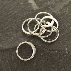 May include: A set of six silver jump rings, stacked and arranged in a circular pattern. The rings are smooth and have a polished finish.