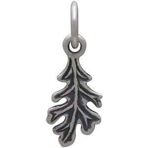 May include: A silver-toned charm in the shape of an oak leaf. The charm has detailed veining and a loop at the top for attaching to a necklace or bracelet. The leaf design is a nature-inspired element.