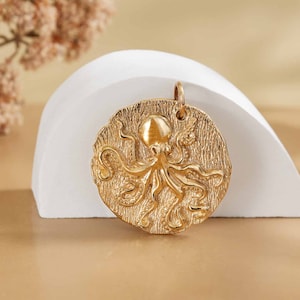 Peut inclure: Un pendentif en or avec un motif d'octopus détaillé. Le pendentif est rond et a une surface texturée.