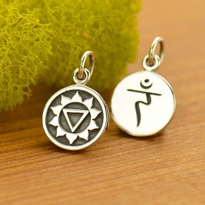 Op de afbeelding: Twee zilveren bedels met een zwart ontwerp. Een bedel heeft een gestileerd symbool van een zon met een driehoek erin. De andere bedel heeft een gestileerd symbool van een persoon in een yogapose.