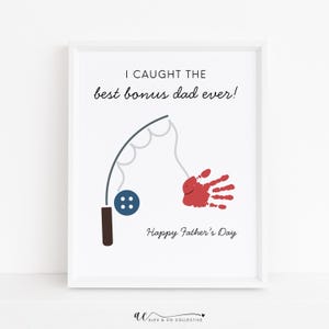 May include: White framed art print with the text "I caught the best bonus dad ever!" and "Happy Father's Day." The print features a fishing rod graphic and a red handprint. A perfect gift for Father's Day.