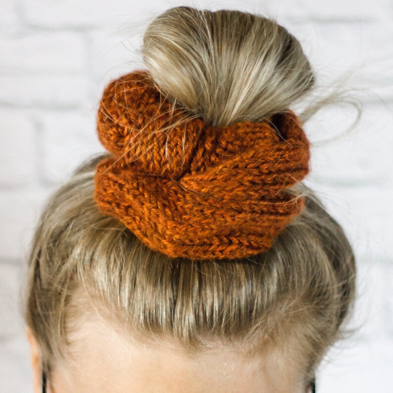 May include: A close-up of a woman's hair styled in a bun with a brown knitted hair scrunchie.