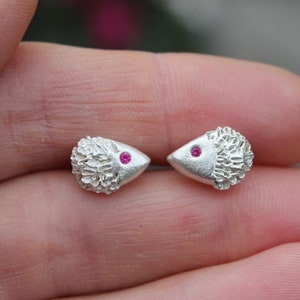May include: A pair of silver earrings shaped like hedgehogs with pink gemstone eyes.