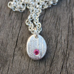 Puede incluir: Un collar de plata con un colgante que presenta un diseño texturizado de tallos de bambú y una piedra preciosa rosa en el centro.