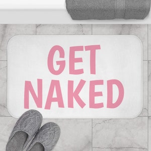 Puede incluir: Alfombra de baño blanca con el texto "GET NAKED" en letras rosas.