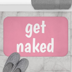 Puede incluir: Alfombra de baño rosa con el texto "get naked" en blanco.