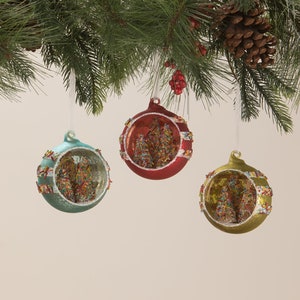 May include: Three glass Christmas ornaments with a glittery, snow-covered scene inside. The ornaments are red, blue, and gold with white stripes.