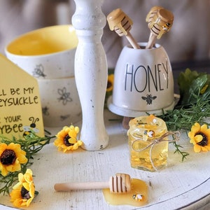 May include: A white tiered tray with a honey-themed decor. The tray features a sign that says "You'll be my honeysuckle, I'll be your honeybee", a honey jar with bees, a honey dipper, and a white ceramic jar that says "Honey". The tray is decorated with yellow flowers and greenery.
