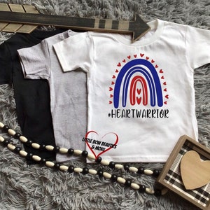 May include: White t-shirt with a red, white, and blue rainbow design and the text "#HEARTWARRIOR".
