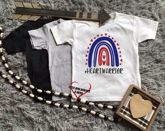 May include: White t-shirt with a red, white, and blue rainbow design and the text "#HEARTWARRIOR".