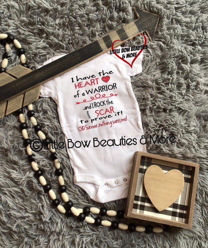 May include: White baby onesie with the text "I have the HEART of a WARRIOR...and I ROCK the SCAR to prove it! CHD Survivor-nothing scares me!"  A red heart is next to the word "WARRIOR". The onesie is on a gray fuzzy surface with a black and white beaded necklace and a wooden box with a black and white plaid design and a wooden heart inside.