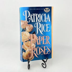 May include: A paperback copy of the book "Paper Roses" by Patricia Rice. The cover features a blue background with a large white and pink rose design.