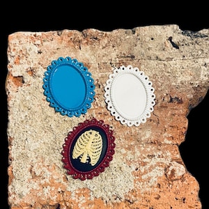 May include: Three decorative metal embellishments with scalloped edges. The embellishments are in the shape of a circle and feature a blue, white, and black background with a white ribcage design.