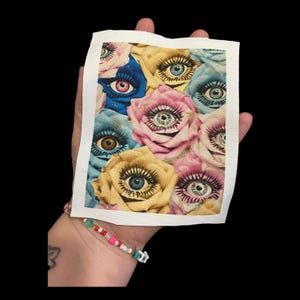May include: A close-up of a colorful fabric print featuring multiple roses with eyes in the center of each flower. The roses are in shades of pink, blue, yellow, and brown.
