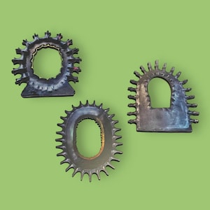May include: Three metal gears with a decorative, sunburst design. Each gear has a different shape and size, with a circular hole in the center.