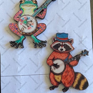 May include: Two wooden figurines, a frog and a raccoon, playing banjos. The frog is green with red and white spots, and the raccoon is brown with a black mask and a blue hat.