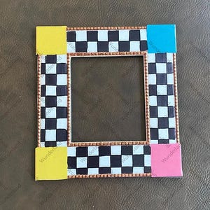 May include: A black and white checkered picture frame with a gold trim. The frame has a yellow, blue, and pink border.