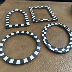 May include: Four decorative coasters in various shapes: an arch, a square, and two circles. Each coaster features a black and white checkered pattern, offering a classic and versatile design. The coasters are displayed on a brown surface.