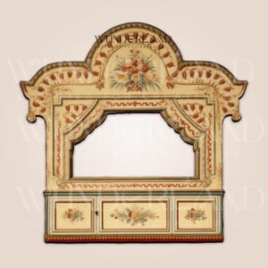 May include: A vintage-style wooden puppet stage with a painted floral design. The stage has a large opening for puppets and a lower section with three drawers. The stage is painted in shades of cream, red, and green.