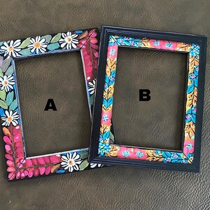 May include: Two black picture frames with colorful floral designs. The frames are side by side, with the frame on the left labeled "A" and the frame on the right labeled "B".