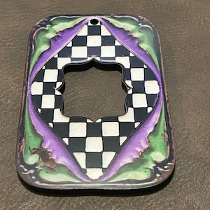 May include: A black and white checkered pattern with purple and green accents. The pattern is framed by a decorative border. There is a hole in the center of the ornament.