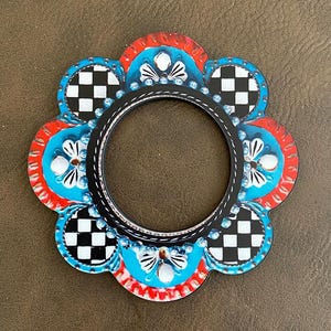 May include: A black and white checkered flower-shaped frame with blue and red accents. The frame has a round opening in the center.