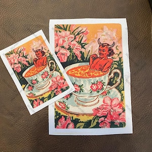 May include: Two stickers featuring a devil relaxing in a teacup. The devil is red with horns, and the teacup is decorated with floral patterns. The background is filled with pink flowers and a yellow sky. The text "Wunderland" is printed on the edges.