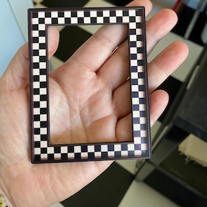 May include: A black and white checkered picture frame with a brown border. The frame is made of plastic and has a smooth finish.