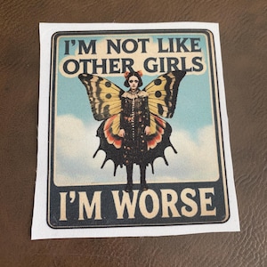 May include: A rectangular patch with the text "I'M NOT LIKE OTHER GIRLS I'M WORSE" in white letters. The image features a woman with butterfly wings against a blue sky background.