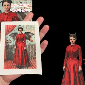 May include: A vintage print of a woman in a red dress with devil horns and wings. The print is on a white background with a red curtain and stars in the background.