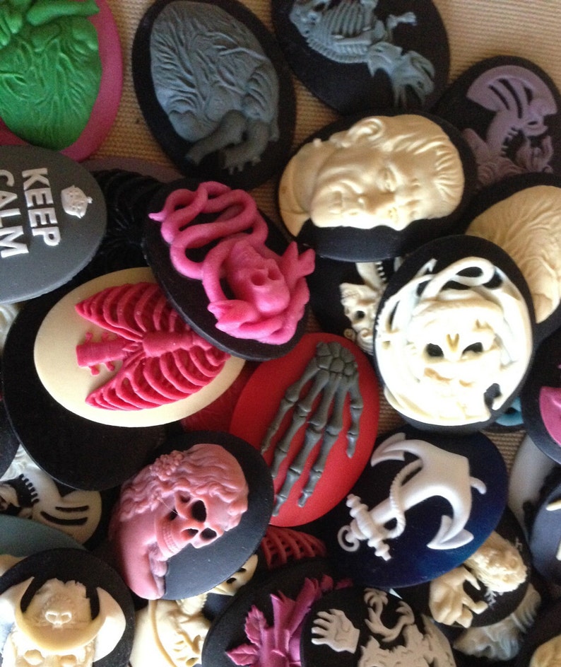 May include: A collection of 18 vintage-style cameo pendants with various designs, including anatomical hearts, skeletons, skulls, and a mermaid. The pendants are made of white and black resin and have a glossy finish.