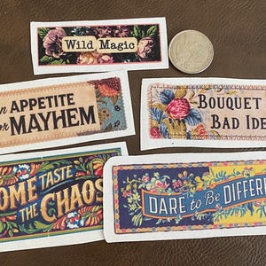 May include: A collection of decorative rectangular stickers with floral and text designs. The stickers feature phrases like "Wild Magic," "An Appetite for Mayhem," and "Dare to Be Different." A coin is also present.